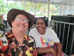 A man in a hat sits next to a smiling young woman with intellectual disabilities