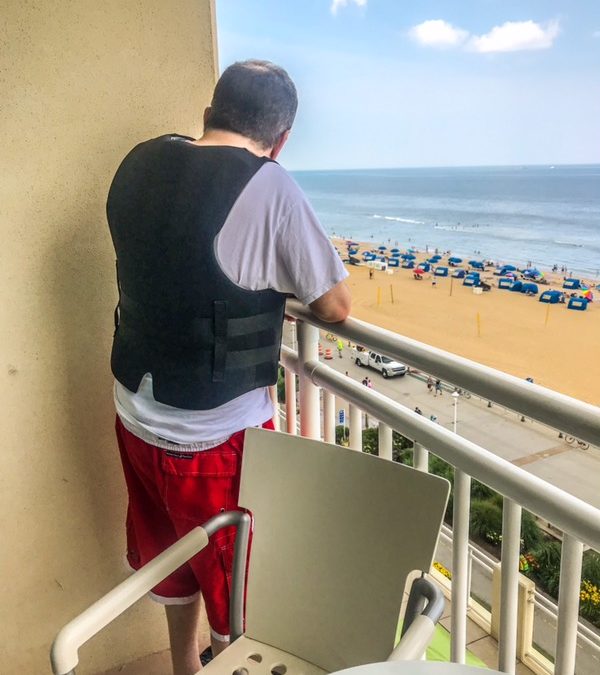 Man in a weighted vest looking over a balcony at the beach