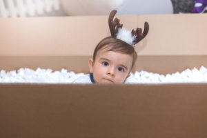 Baby wearing reindeer antlers is in an empty shipping box.