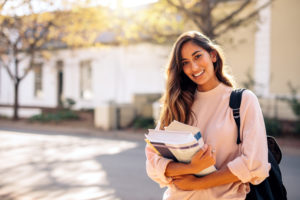 Beautiful young woman with backpack and books outdoors. College student carrying lots of books in college campus.