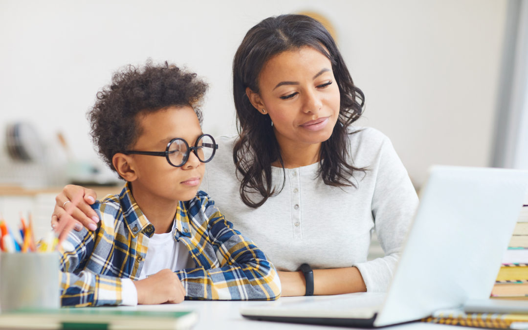 Portrait of cute African boy wearing big glasses while using laptop with mom, homeschooling and remote education concept