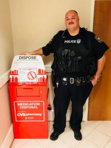 Police officer stands beside red bin for medication disposal