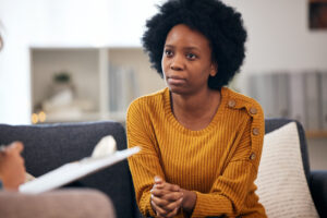 Woman sits on chair talking to someone making notes on a clipboard