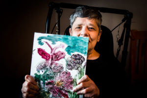 Woman in a wheelchair holds colorful painting of butterflies