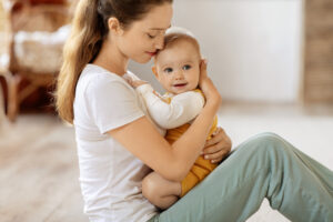 Young woman with long ponytail cuddles a smiling baby