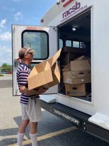 A man loads cardboard boxes into the back of a white van that says RACSB