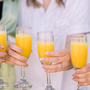 Girls are celebrating the bride with mimosas and orange juice in champagne glasses.