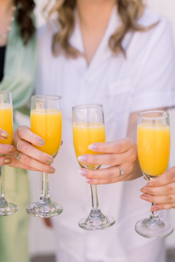 Girls are celebrating the bride with mimosas and orange juice in champagne glasses.