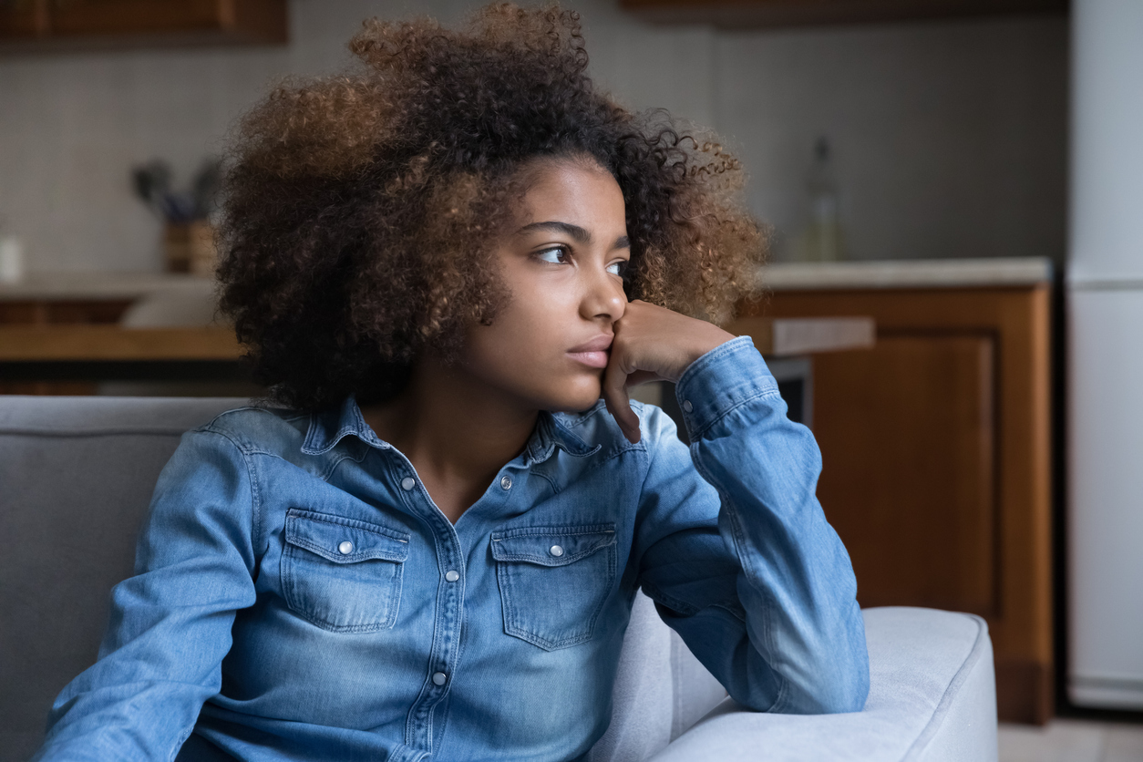d pensive teenage African girl sitting on couch at home, looking away