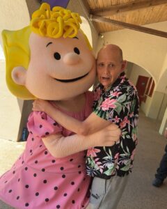 A middle-aged white male with developmental disabilities poses with someone dressed up as Lucy from Snoopy at Kings Dominion