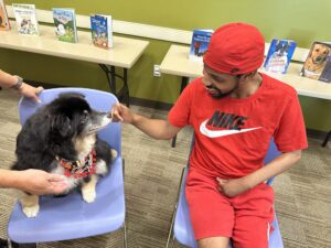A young adult, black man with disabilities pets a puppy in a library