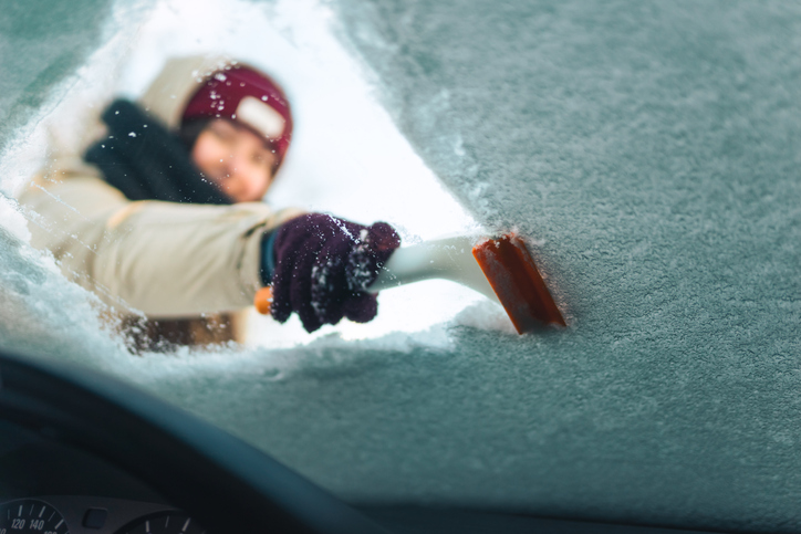 Woman cleans windshield with ice scraper in winter storm