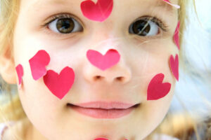 Close up of face of toddler with red heart stickers all over face