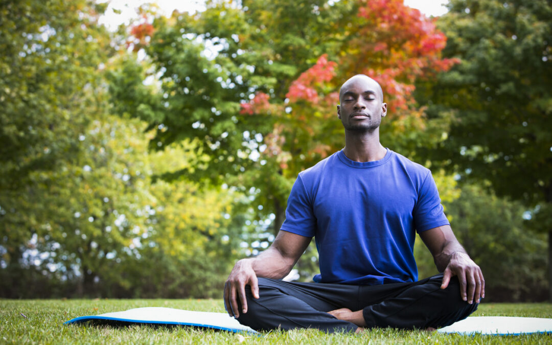 young black man wearing athletic wear sitting in the park exercising yoga