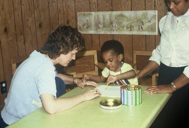 A faded vintage photo shows a woman and a toddler coloring with crayons