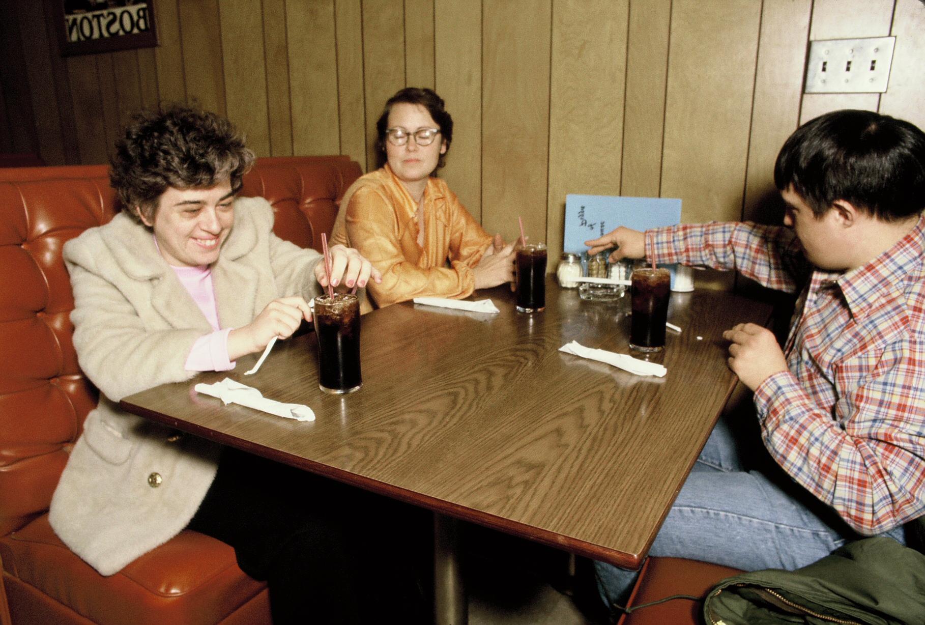 Three young adults with developmental disabilities sit at a table in a casual restaurant
