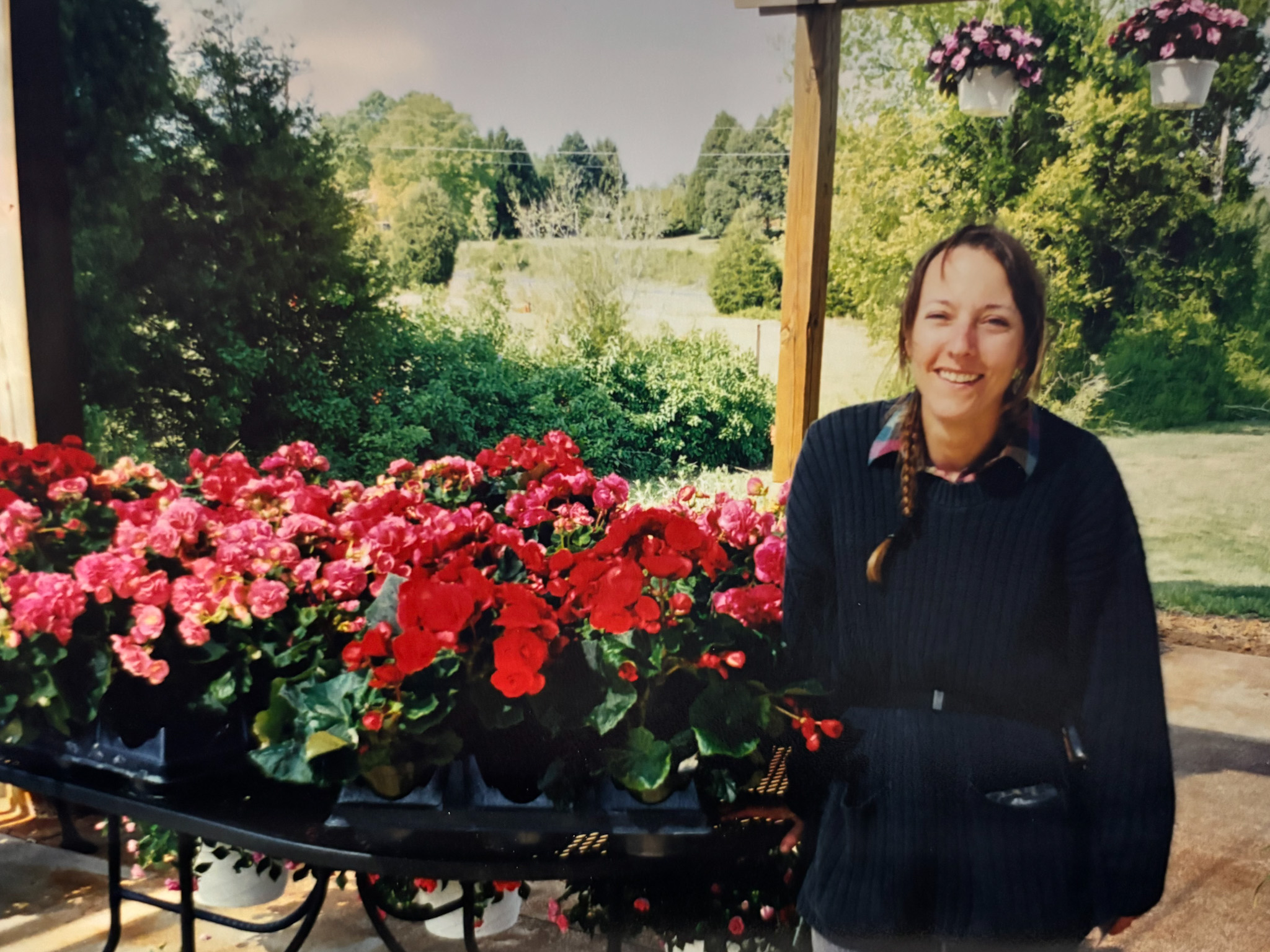 A woman with a braid stands in front of a table with potted flowers
