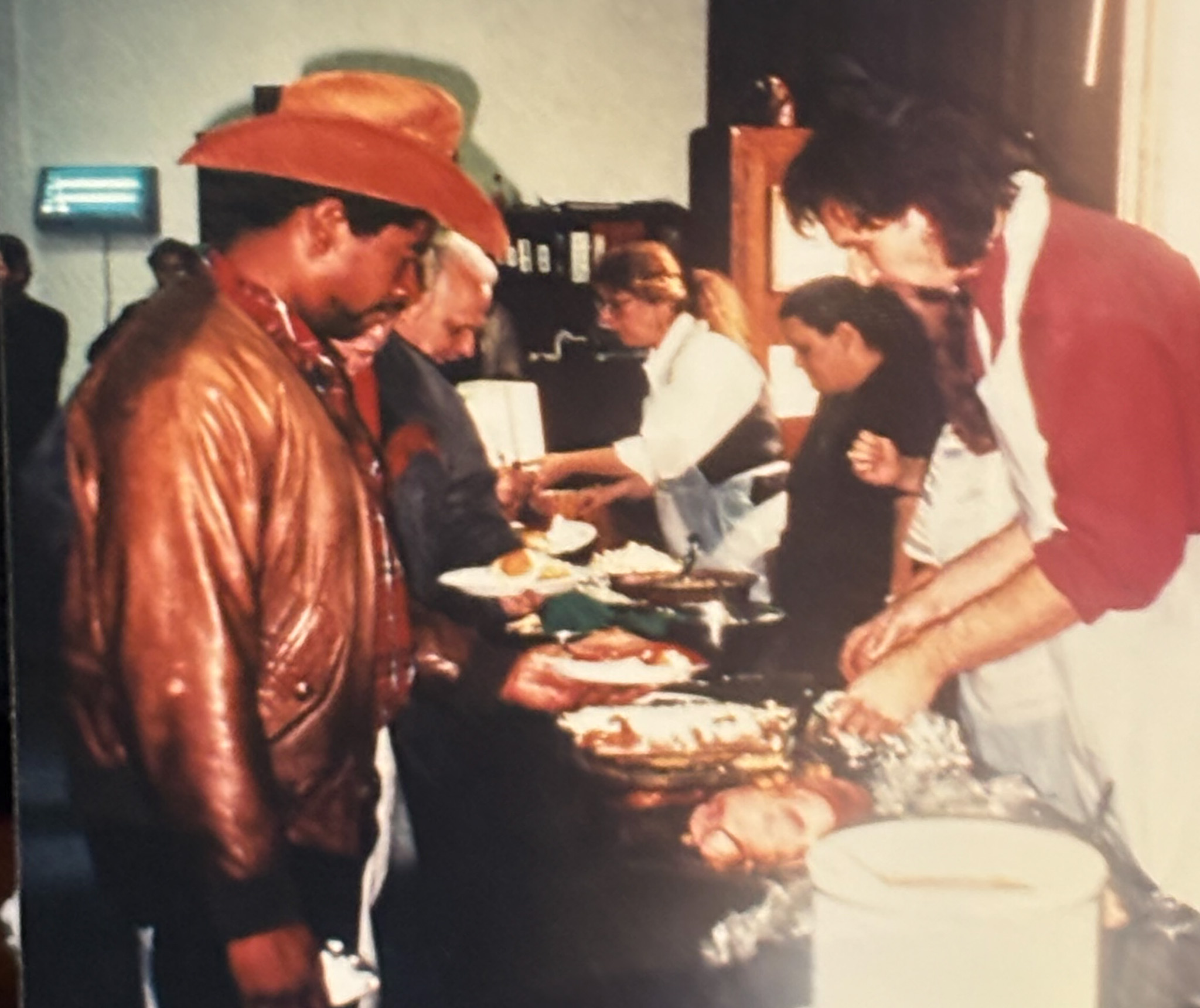 A man wearing a red shirt and white apron serves Thanksgiving lunch to a man wearing a cowboy hat