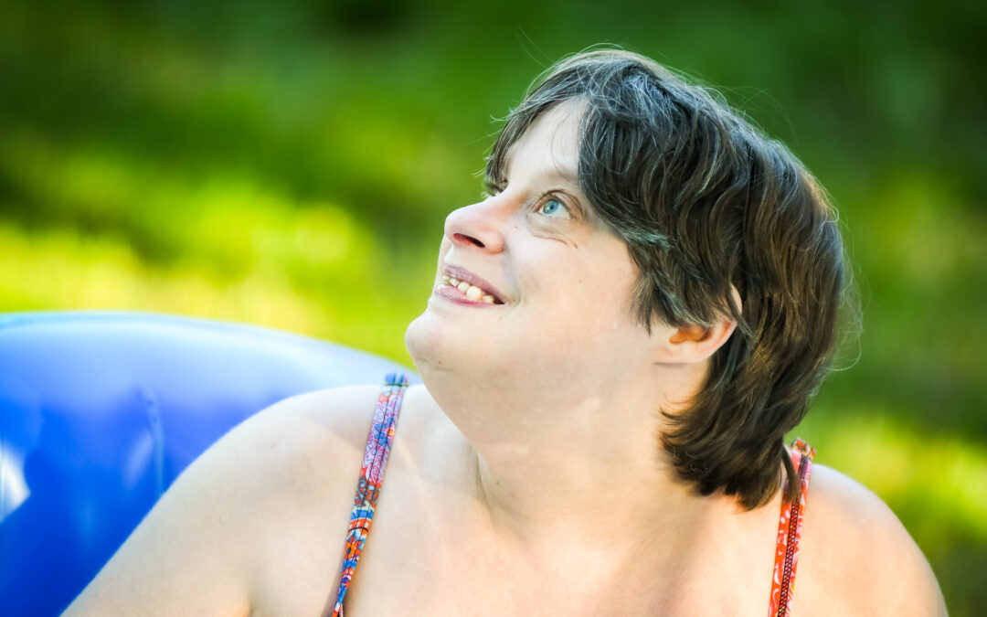 A woman with a developmental disability splashes in a blue inflatable pool