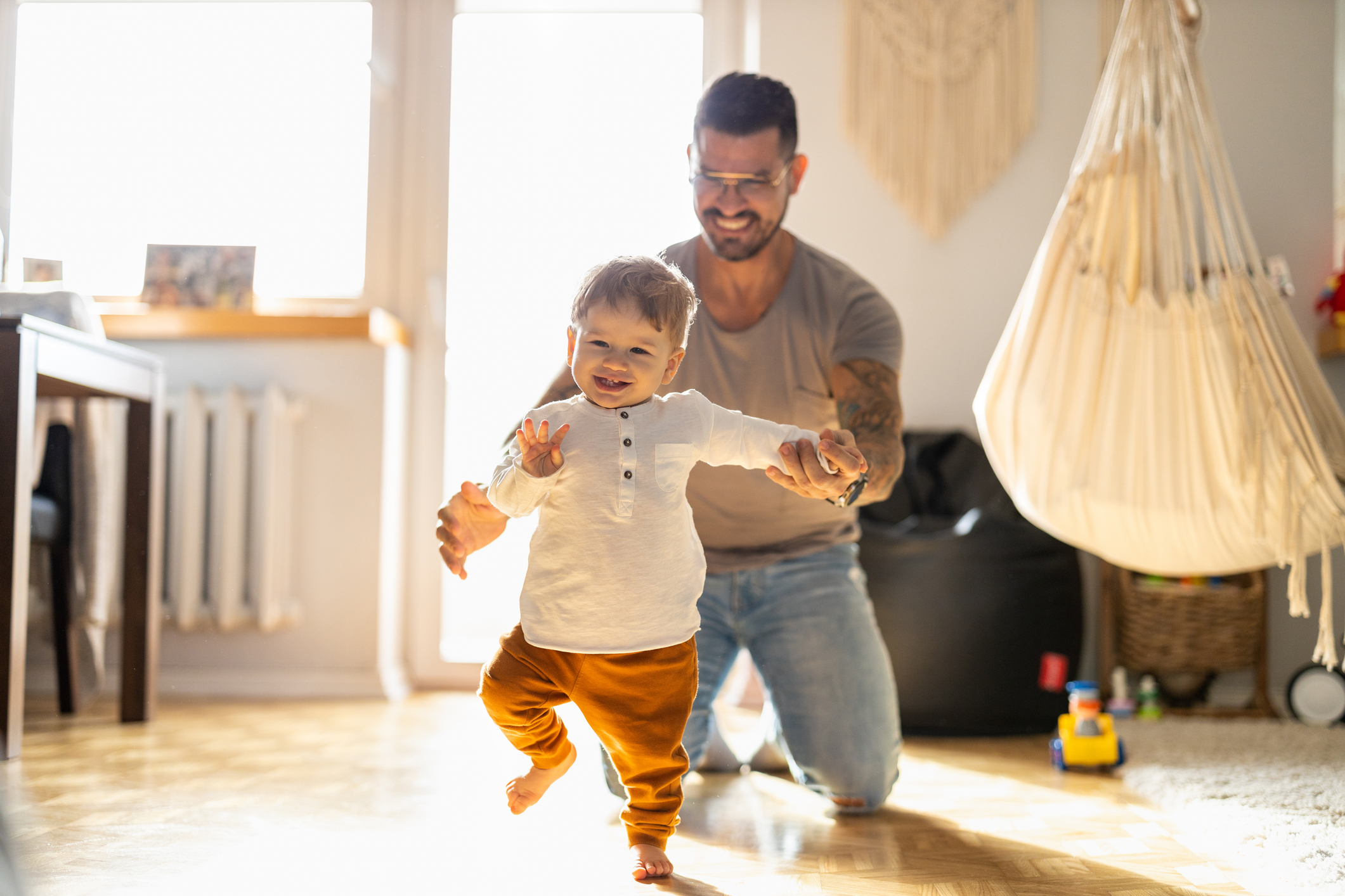 Baby in white shirt takes wobbly steps as dad watches