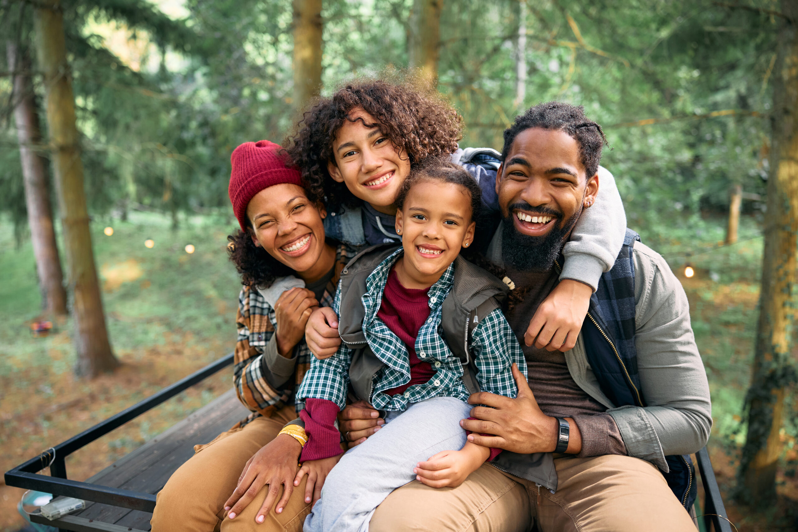 Happy African American parents with kids enjoying in camping at trailer park in the woods and looking at camera.