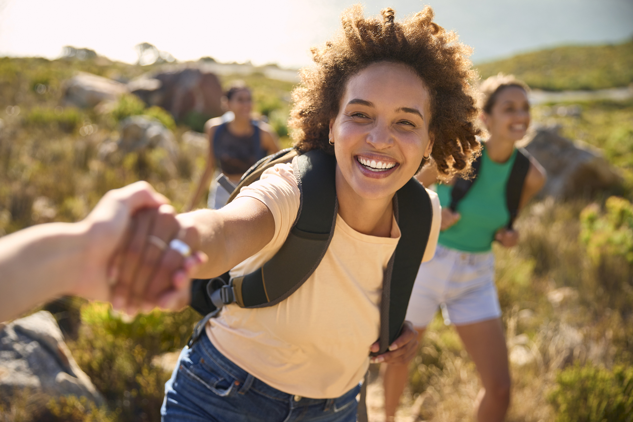 A young woman with a backpack holds her hand to help another woman on a hike 