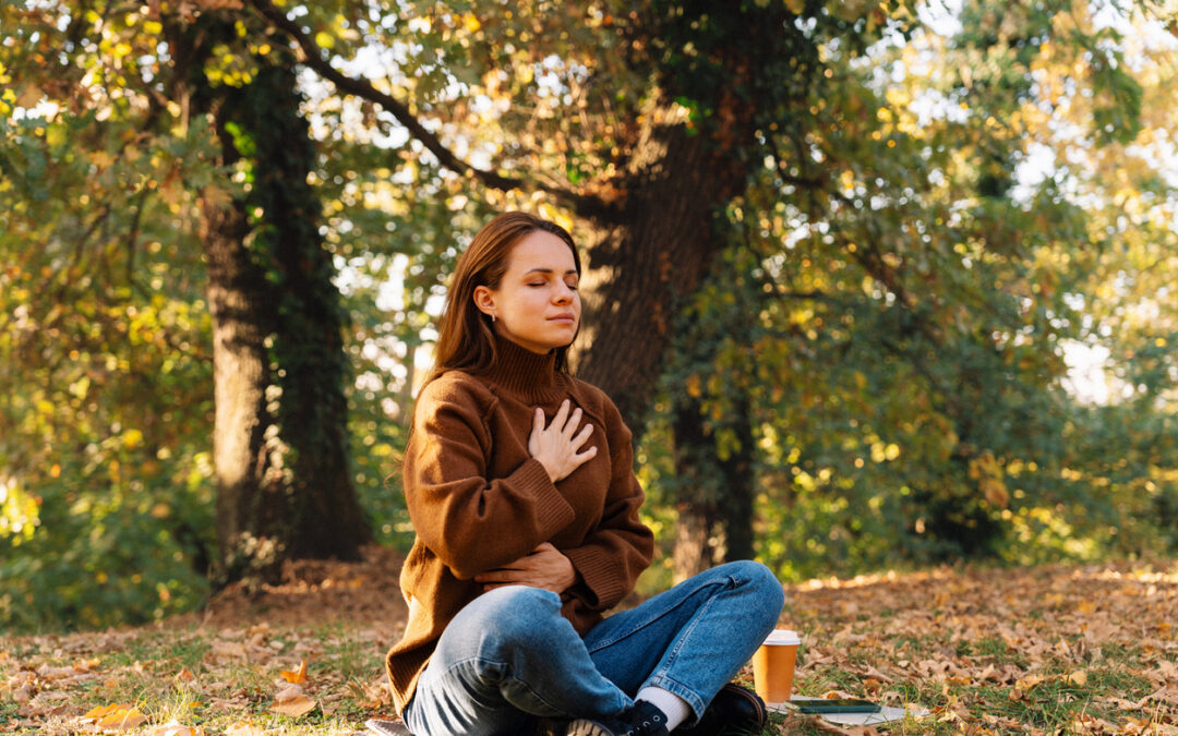 Adult woman practicing deep breathing exercise and mindfulness meditation sitting cross-legged on ground in autumn park